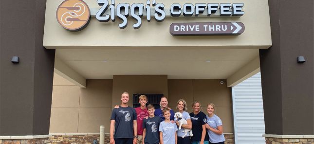 Franchise owned Ziggi’s Coffee drive thru location with the full family of one of Ziggi’s Franchisees standing in front, smiling. The group is wearing Ziggi’s branded apparel, representing the sense of community and family value behind Ziggi’s Coffee franchise opportunities.